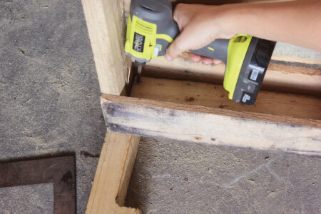 person using electric drill to screw a chair leg to a wood pallet